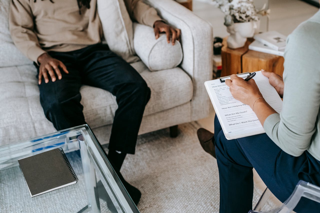 Services-01 From above crop African American male in casual clothes sitting on comfy couch and answering professional female consultant questions in modern psychotherapy office